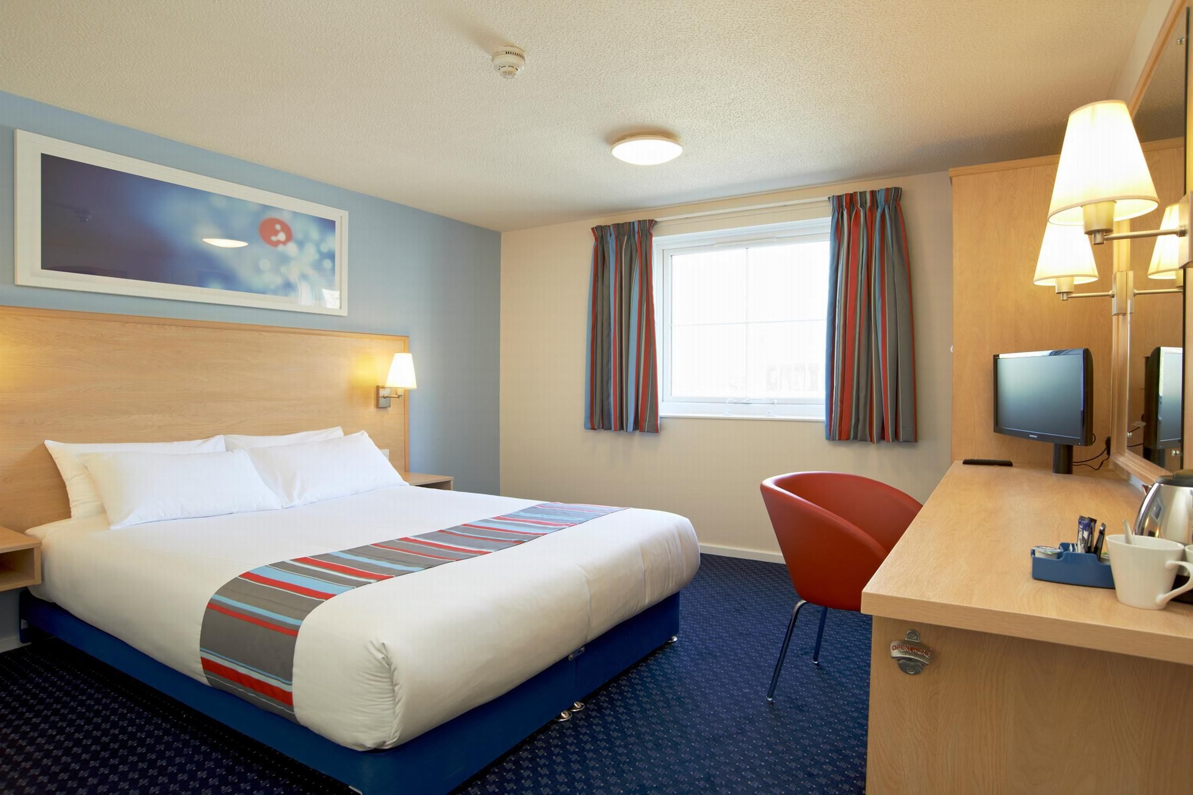 A hotel room with a large bed, a desk with a chair, a television, and a window with curtains.