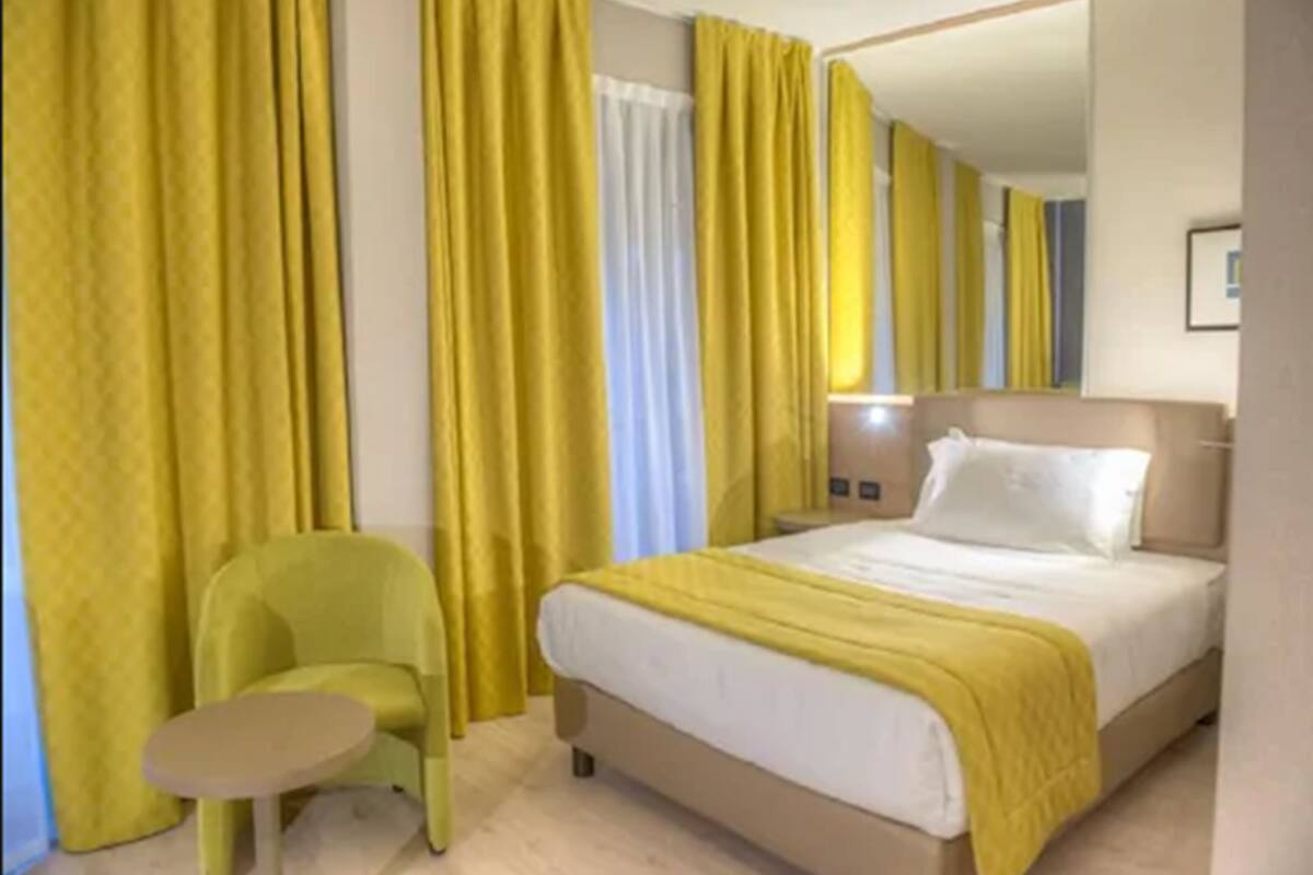 Ein Hotelzimmer mit Bett, Stuhl und Vorhängen.