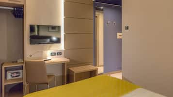 Una habitación de hotel con cama, escritorio, silla, televisor y armario.
