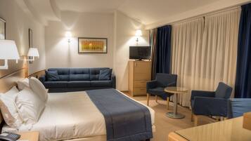 Hotelkamer met een bed, een bank, een bureau, een stoel, een televisie en een raam met gordijnen.