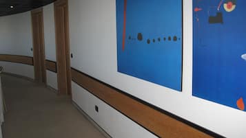 A hallway with a wooden floor, white walls, and a blue artwork on the right.