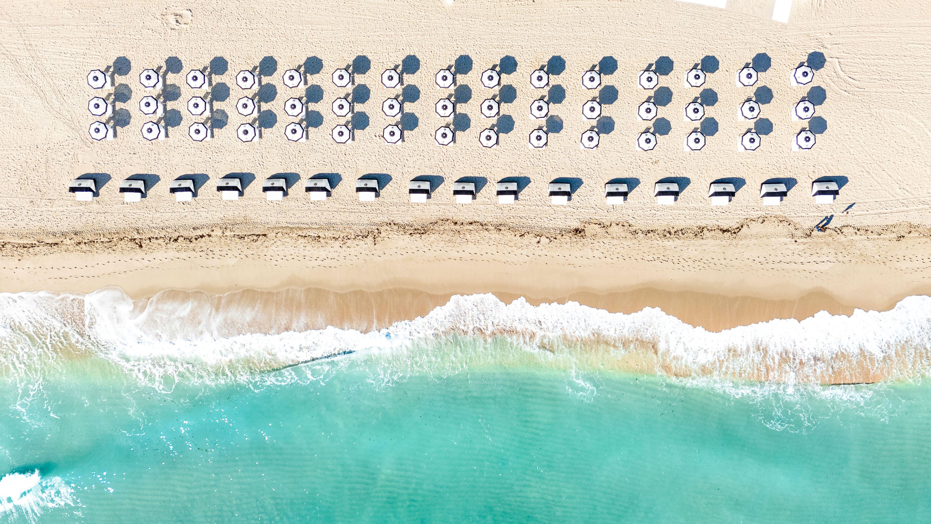 An aerial view of a beach with rows of umbrellas and lounge chairs.