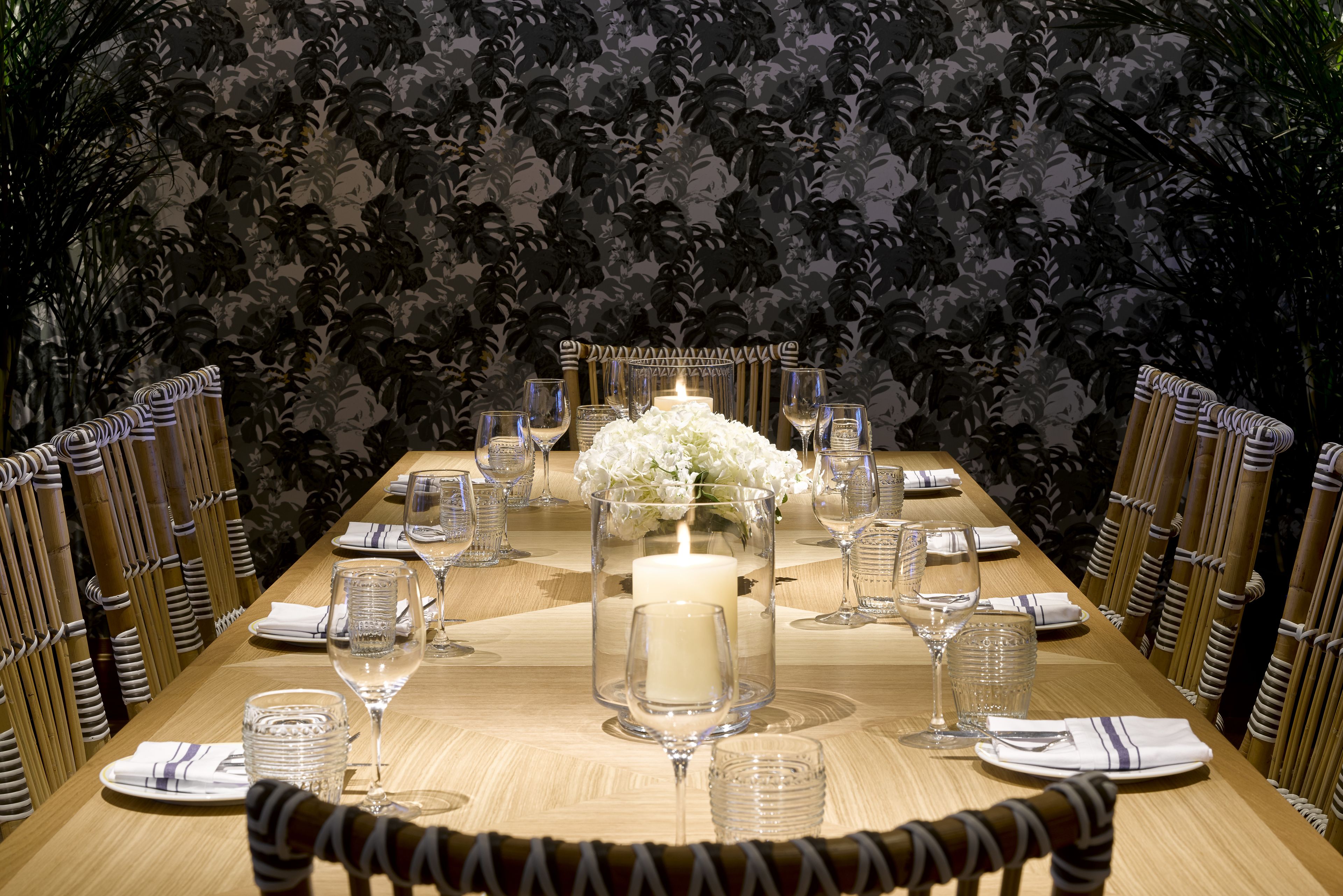 Una larga mesa de comedor dispuesta con cristalería, platos y un centro de mesa con flores blancas y velas.