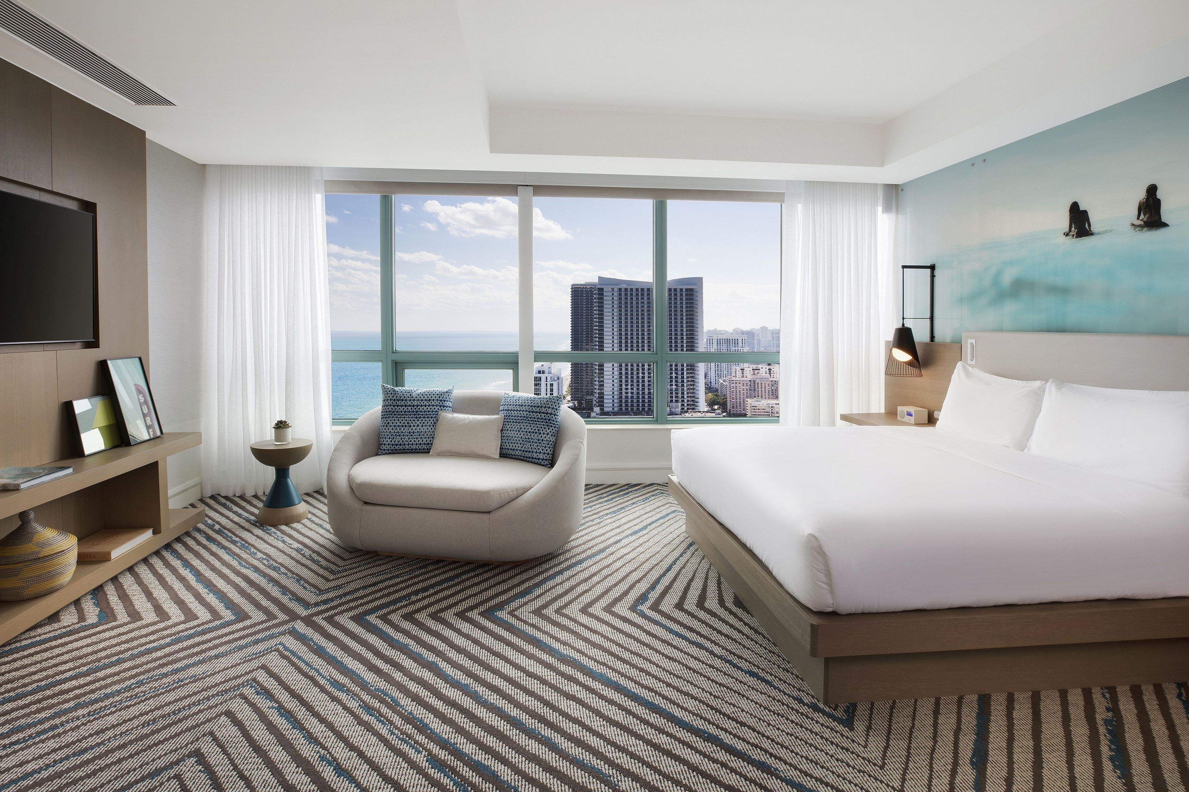 A hotel room with a large bed, a sofa, a TV, a desk, and a view of the city.