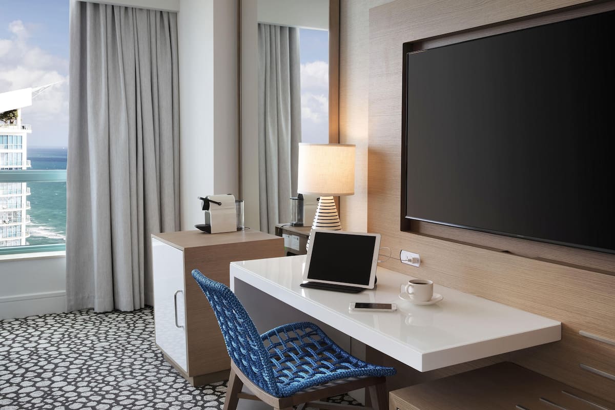 A hotel room with a desk, laptop, smartphone, and a TV.