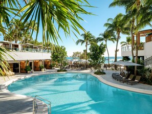 A swimming pool with lounge chairs and umbrellas, surrounded by palm trees and a view of the ocean. - Signia by Hilton Diplomat Beach Resort (Hollywood)