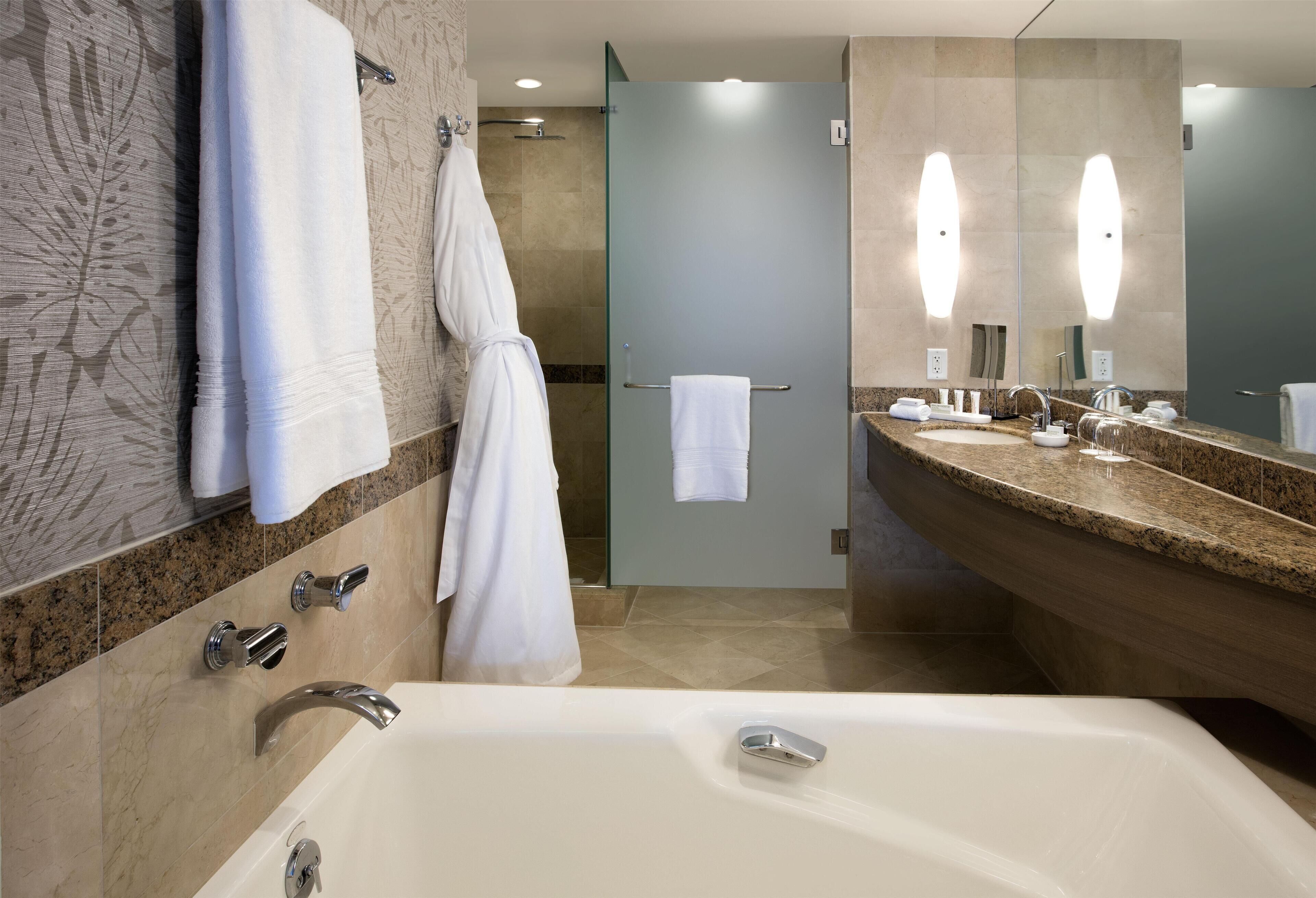 Un baño moderno con bañera, dos lavamanos, mampara de ducha de vidrio y un espejo grande.