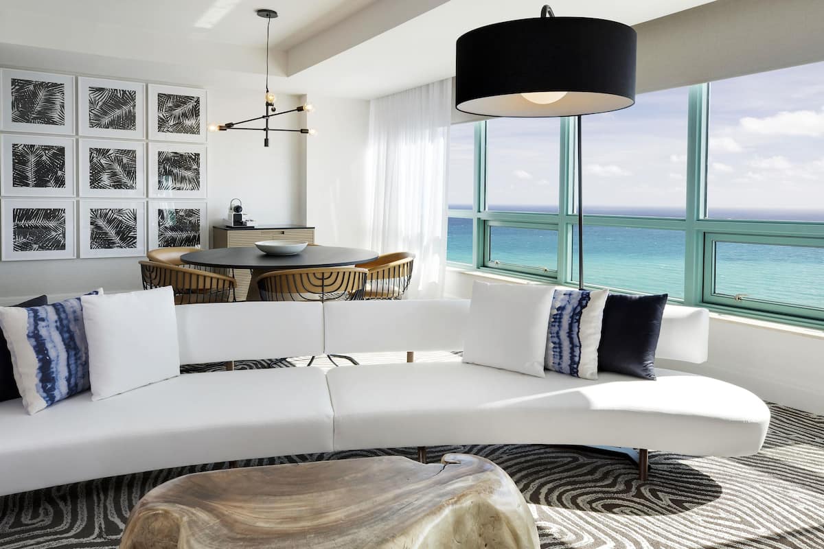 A modern living room with a white sofa, a round coffee table, and a view of the ocean through large windows.