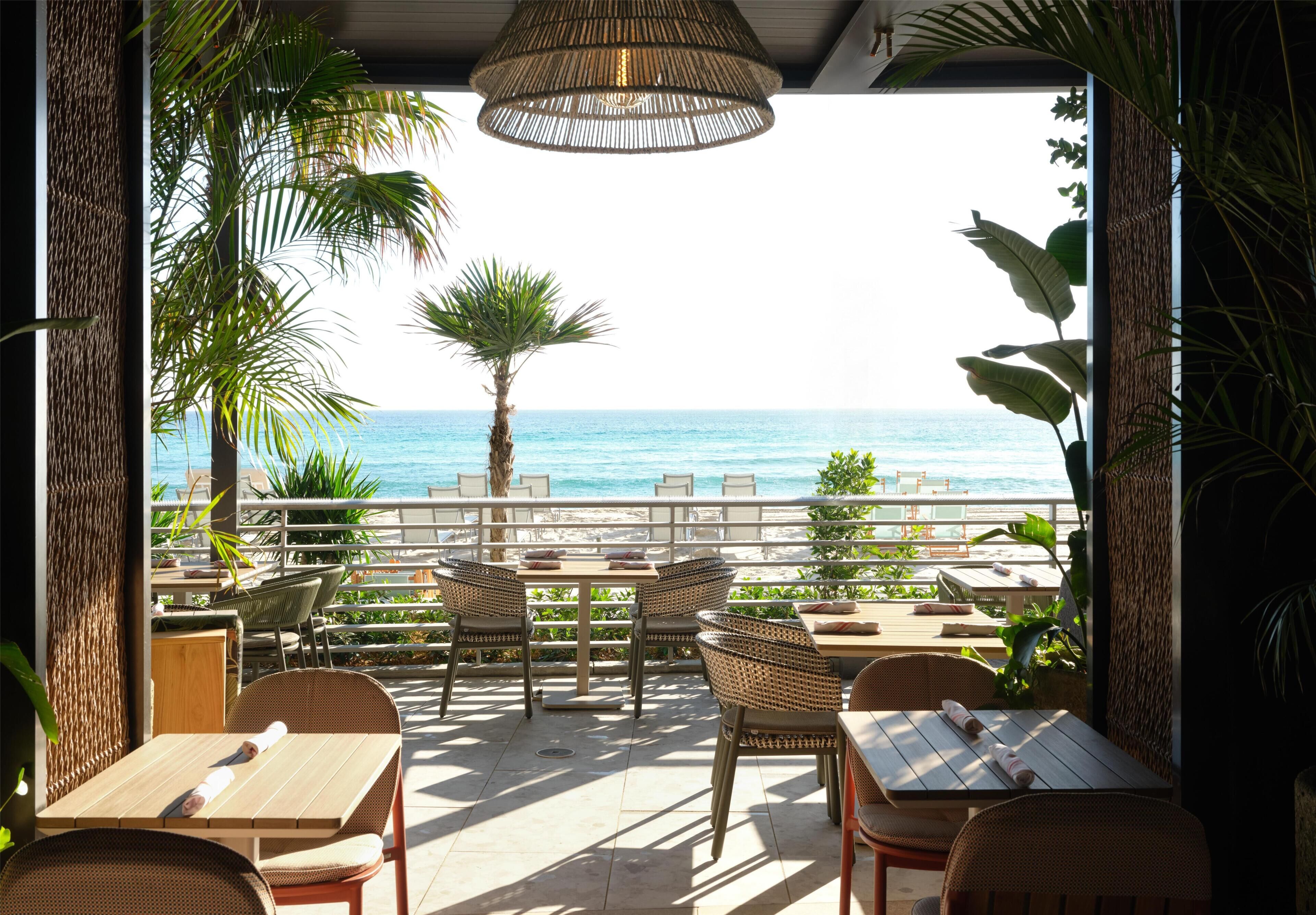 An outdoor seating area with tables and chairs, overlooking a beach.