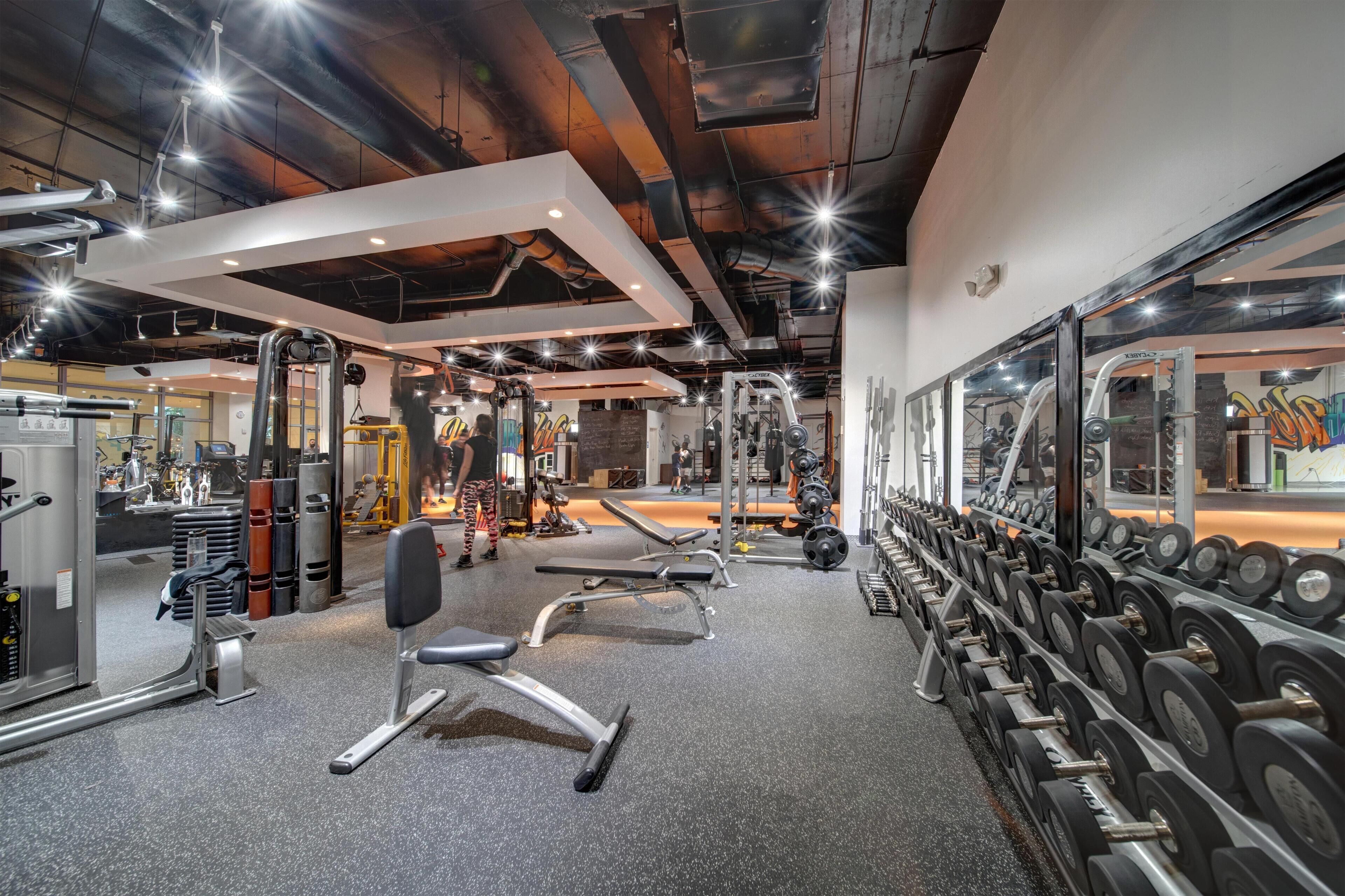 Un gimnasio con equipo de ejercicio, estanterías para pesas y un espejo grande.
