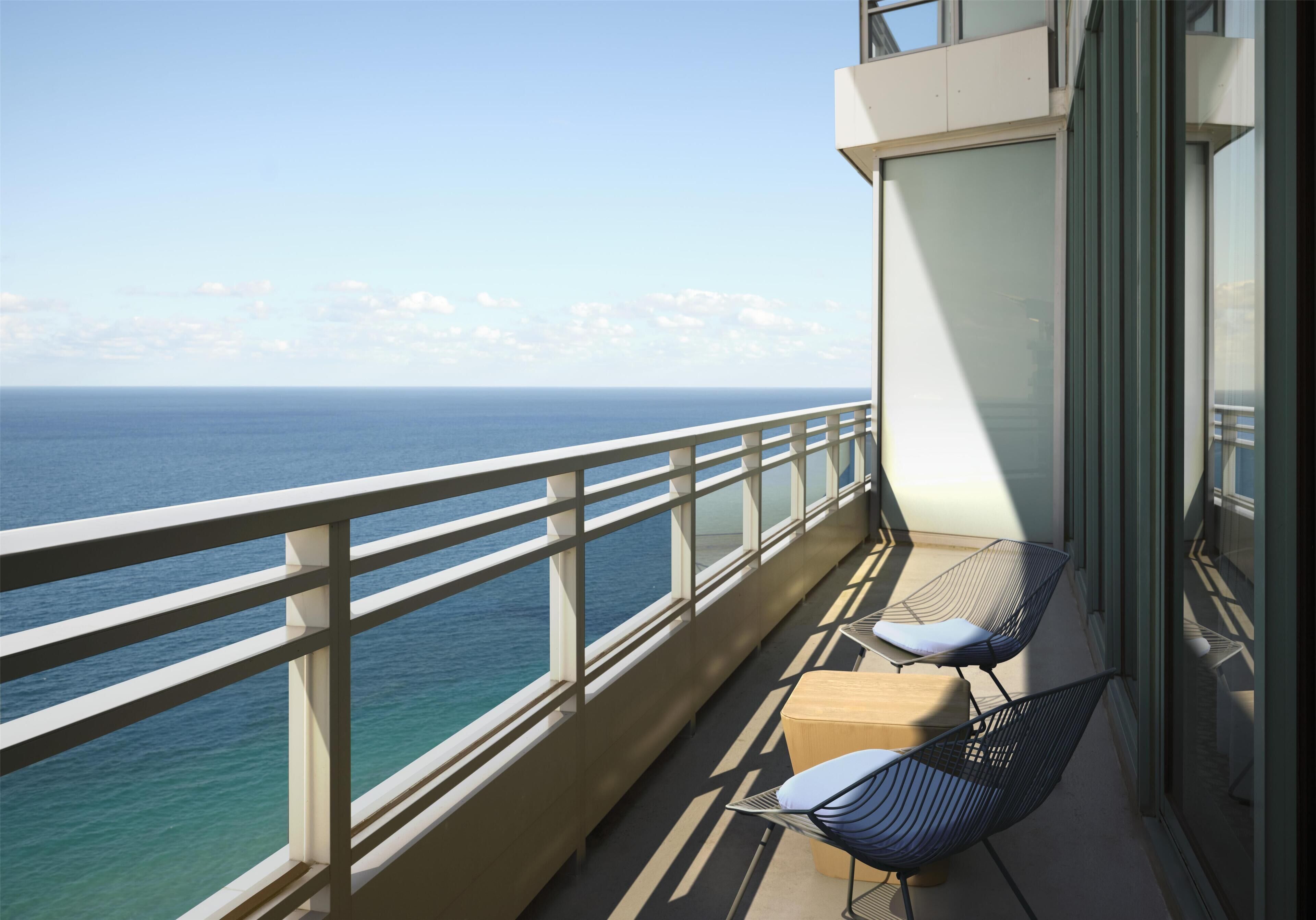 A balcony with a view of the sea, two chairs, and a small table.