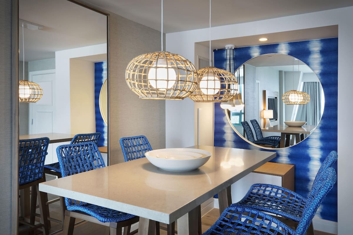 A dining area with a round table, blue woven chairs, and hanging light fixtures.