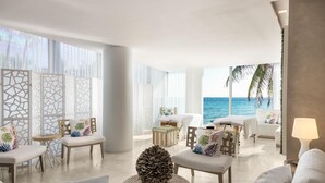 Um quarto espaçoso com vista para o oceano, com área de estar incluindo uma mesa redonda, um sofá e um enfeite de pinhão.