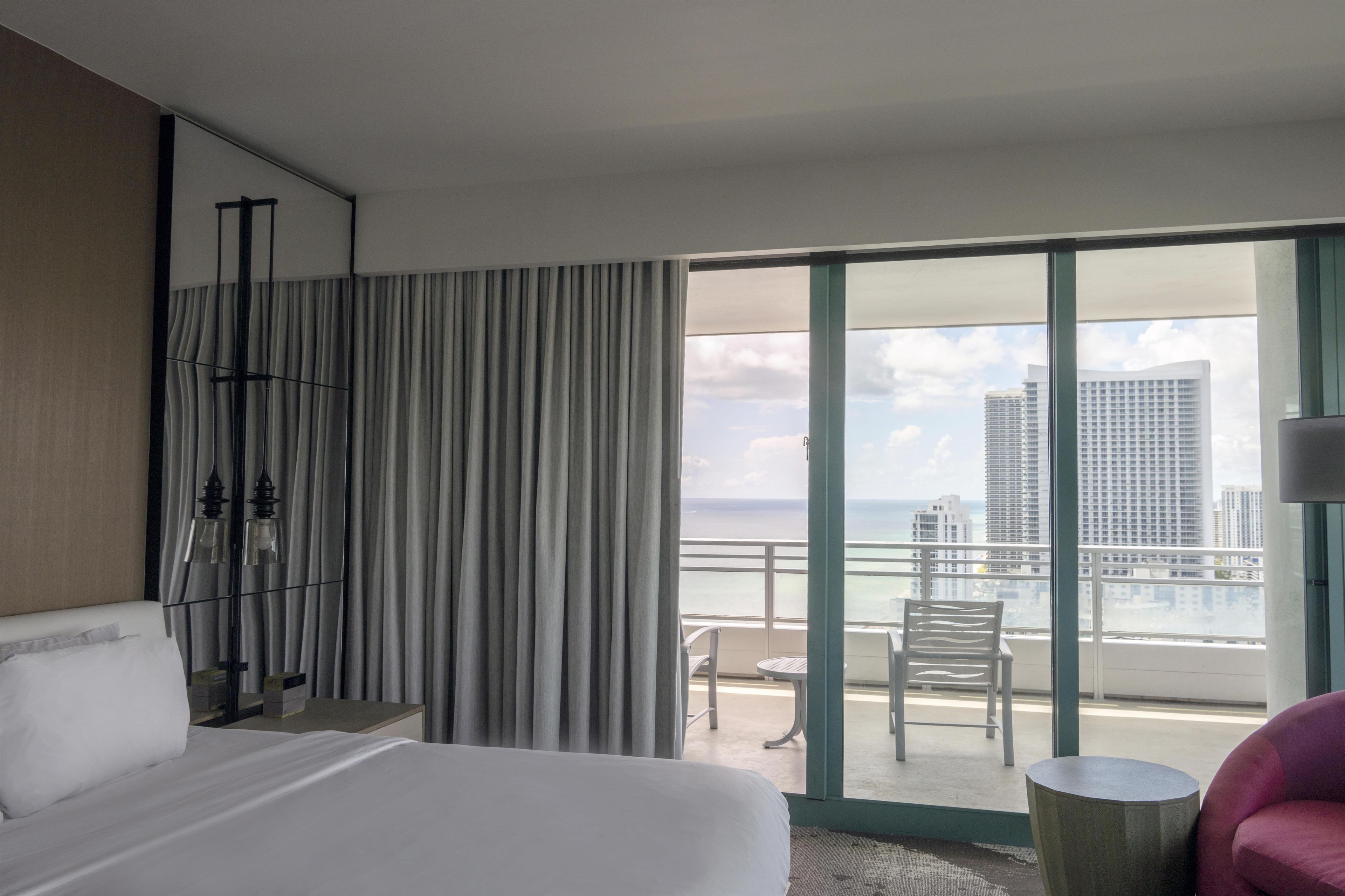 Habitación de hotel con una cama grande, una silla, una mesa y vistas a la ciudad y al océano.