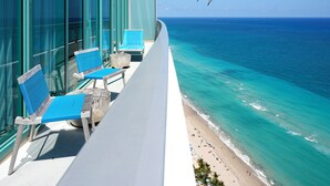 A balcony with two blue chairs and a table, overlooking a beach with clear turquoise waters and a few people in the distance. - Signia by Hilton Diplomat Beach Resort (Hollywood)
