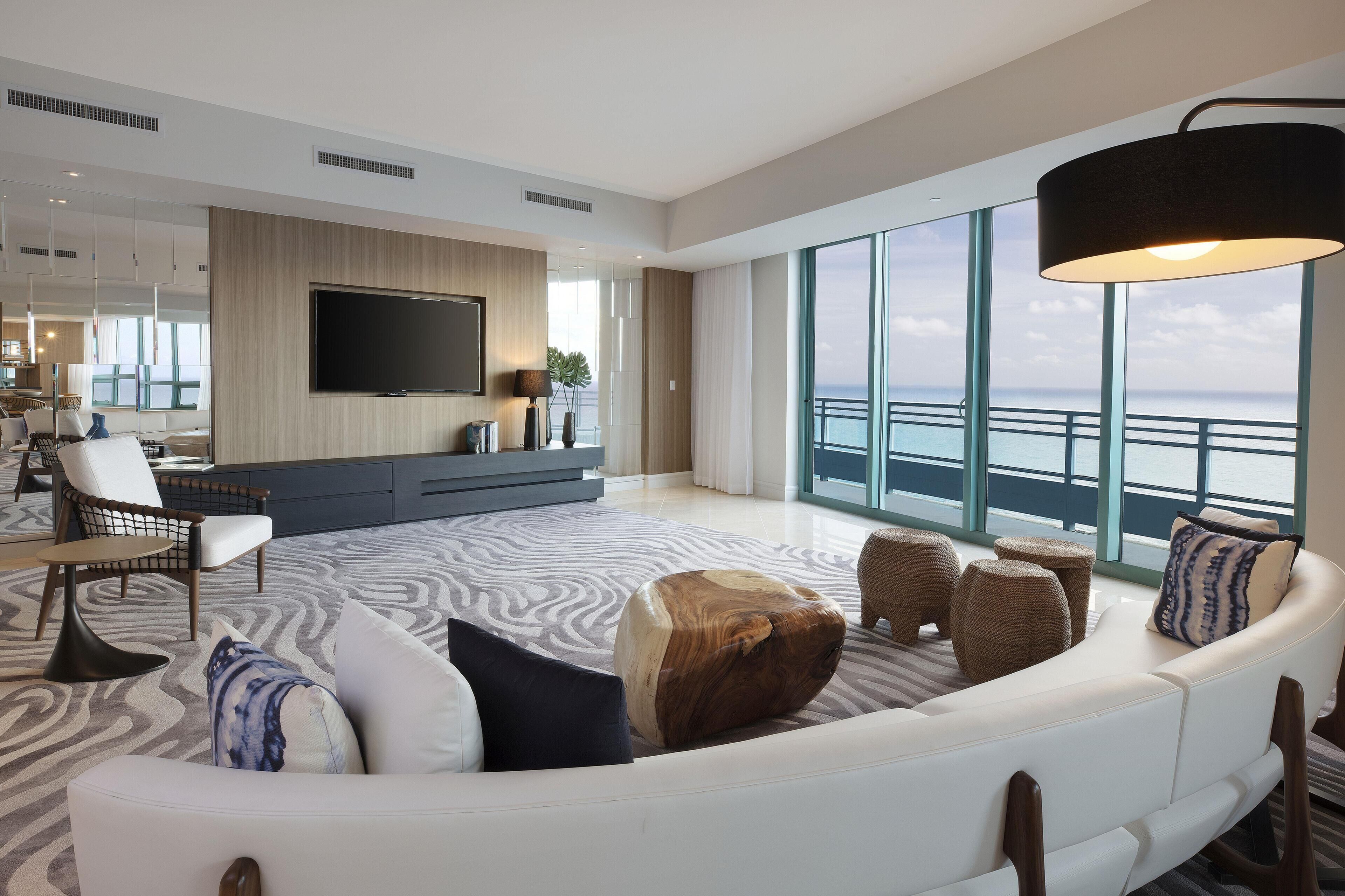 A modern living room with a large sofa, a flat-screen TV, and a view of the ocean.