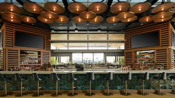 Un bar con varios taburetes, una gran variedad de botellas y un amplio ventanal al fondo.