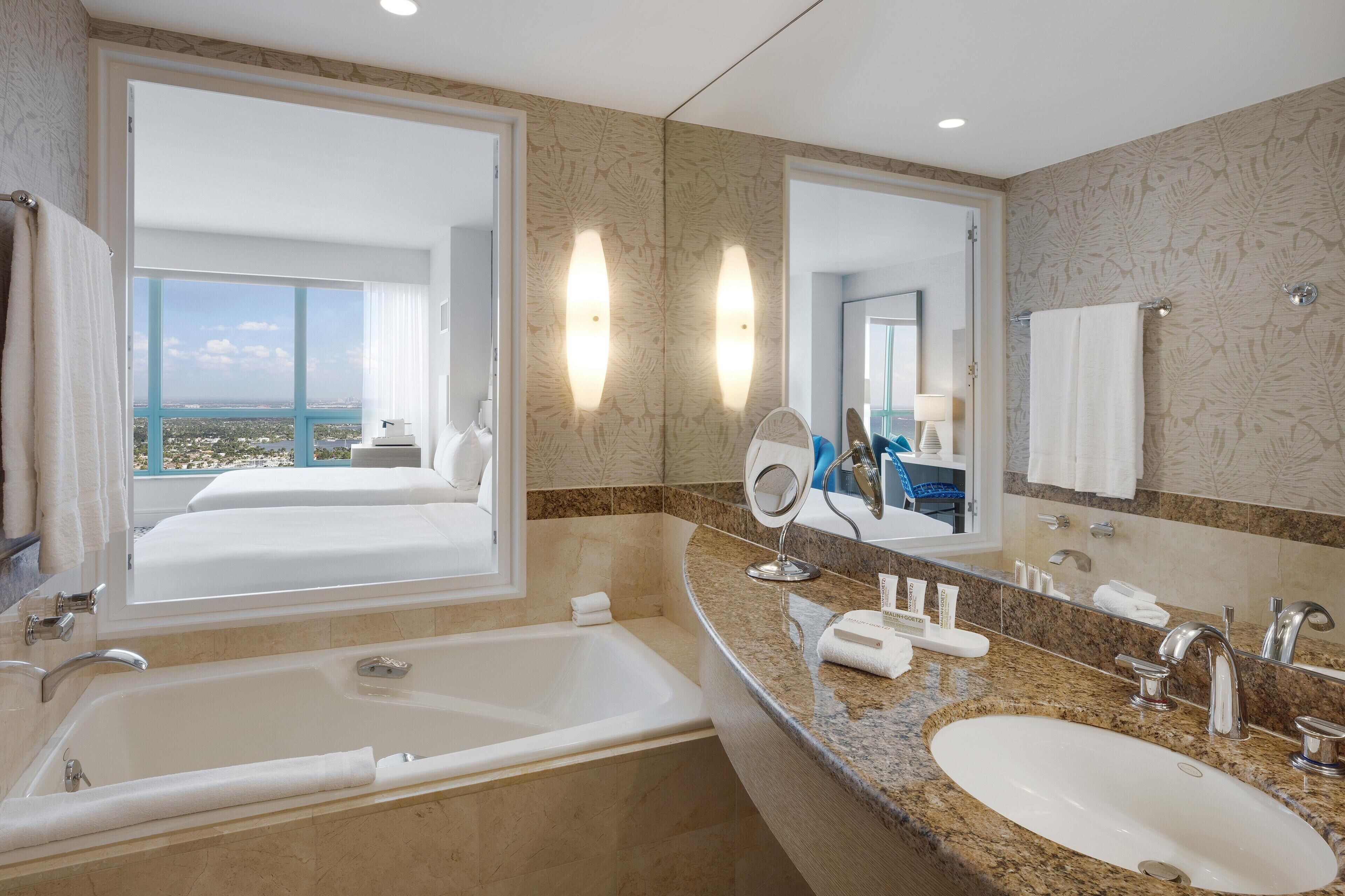 A modern bathroom with a large bathtub, a sink, a mirror, and a view of the city.