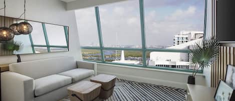A modern living room with a large window, a sofa, two side tables, and a patterned rug.