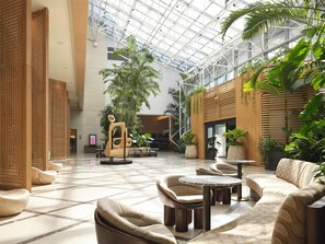 Un vestíbulo amplio con techo alto, mobiliario moderno y exuberantes plantas de interior.