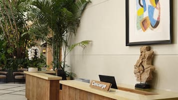 Un comptoir d’accueil avec une pancarte indiquant « Concierge », une sculpture et un tableau abstrait encadré.