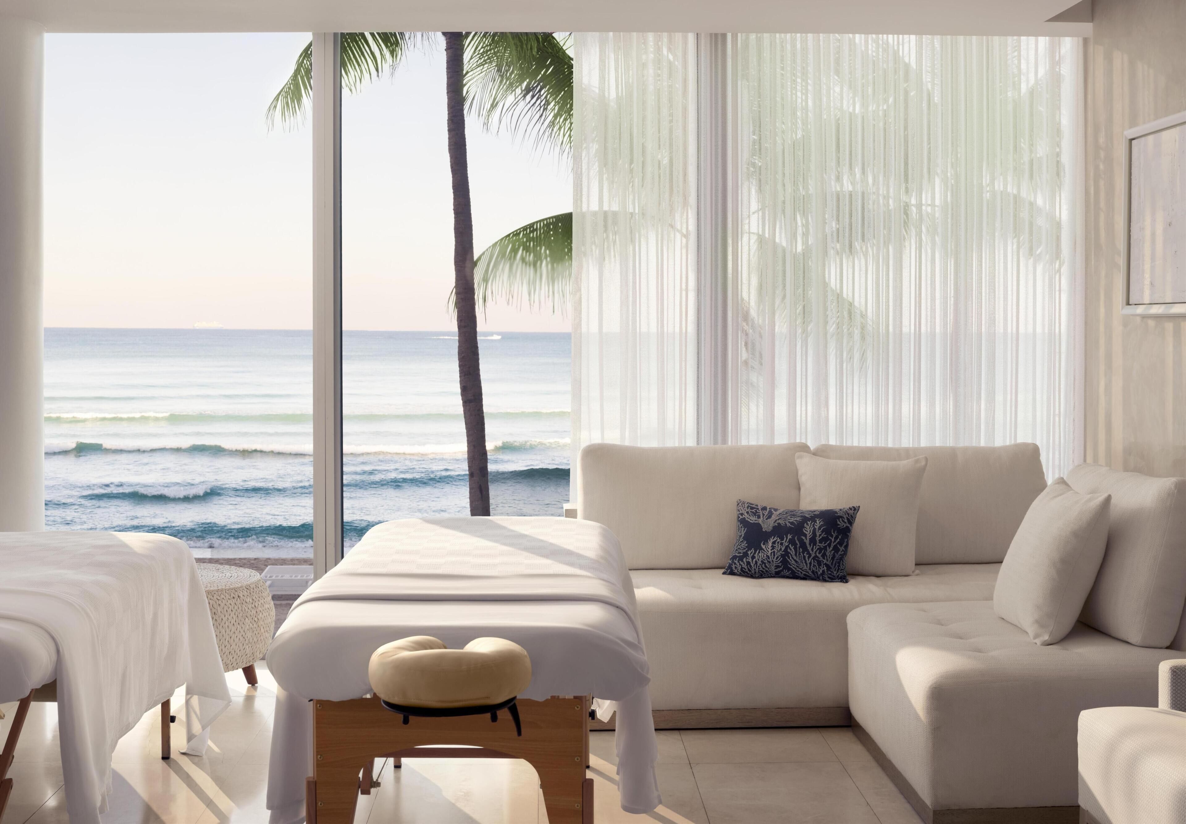 A room with a bed, a massage table, a sofa, and a view of the ocean.
