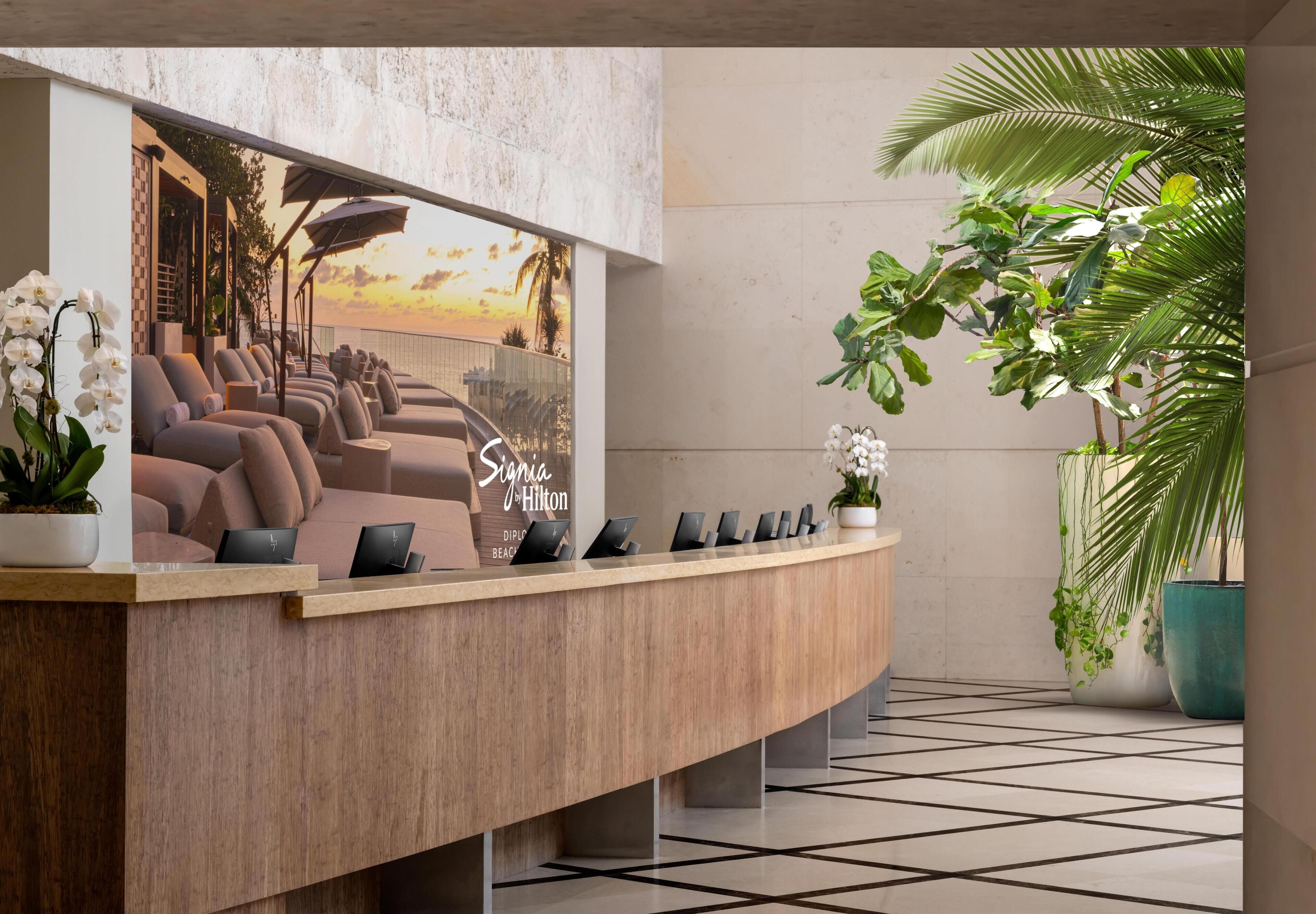 A reception desk with a view of the sunset, a sign for Signia Hilton, and several potted plants.