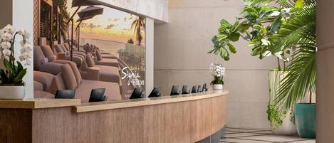 A reception desk with a view of the sunset, a sign for Signia Hilton, and several potted plants.
