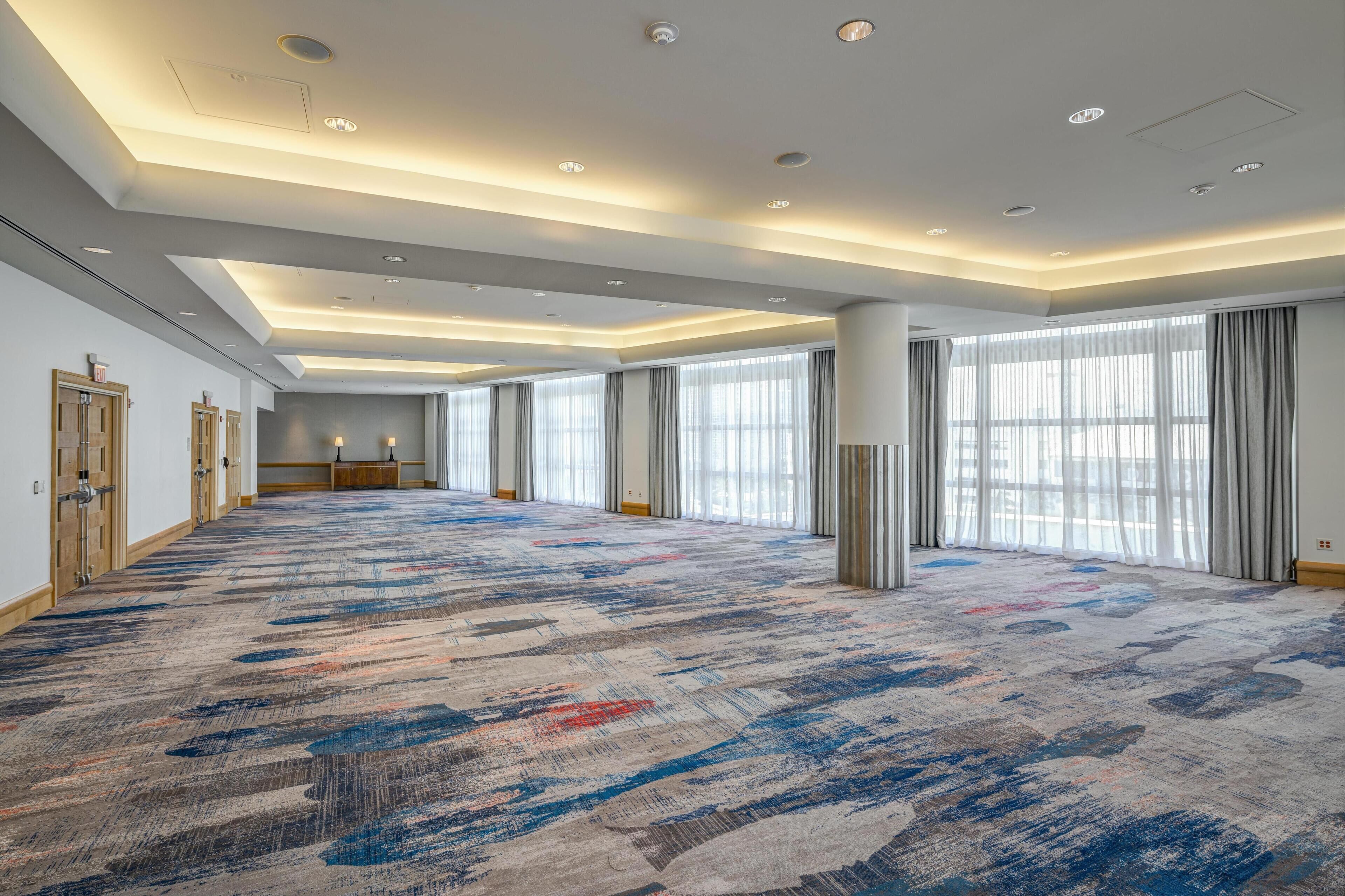 A spacious hotel room with a large carpeted area, large windows with curtains, and a modern ceiling design.