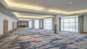 A spacious hotel room with a large carpeted area, large windows with curtains, and a modern ceiling design.