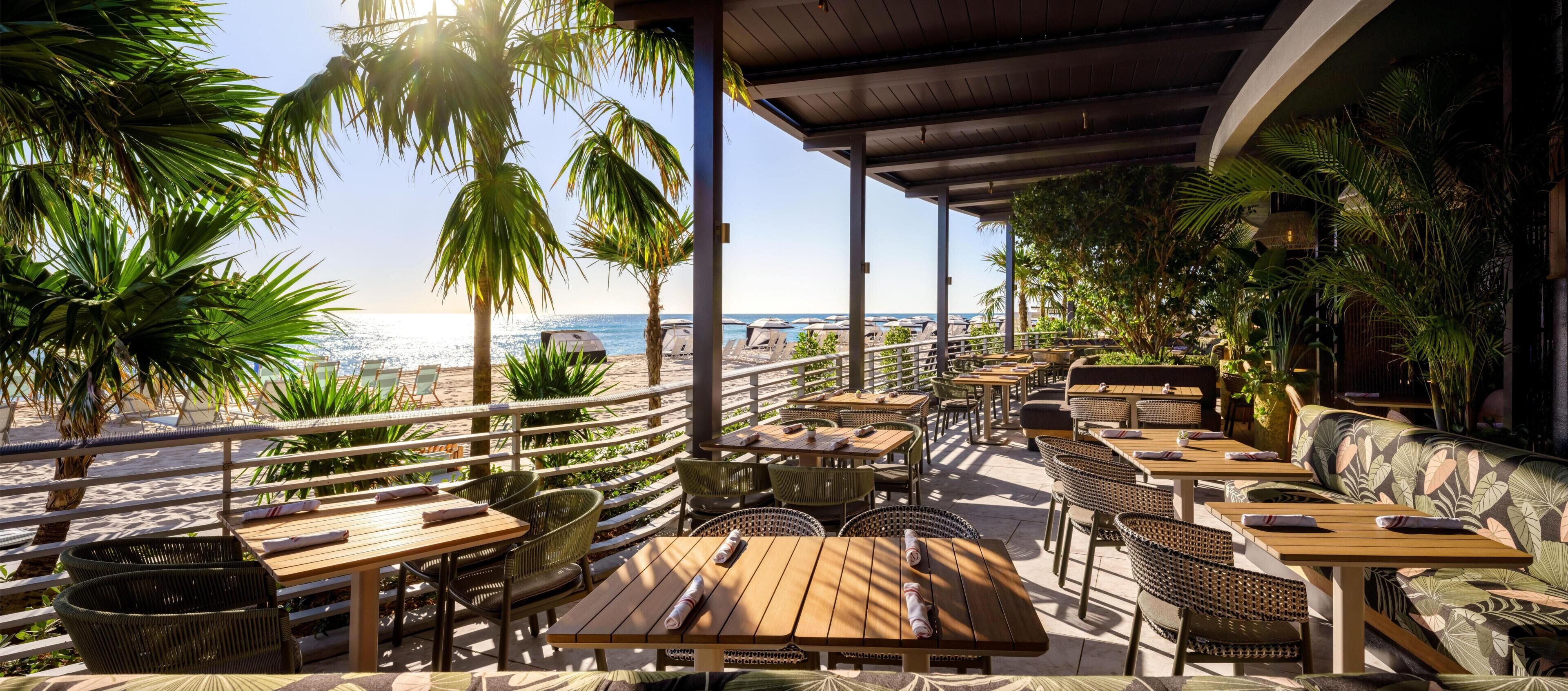 An outdoor seating area with tables and chairs, overlooking a beach and the ocean.
