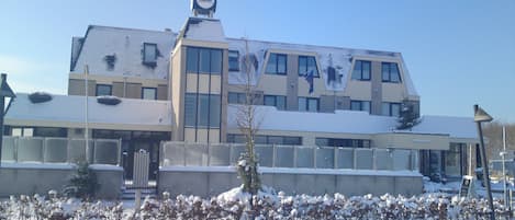 A modern building with a flat roof, large windows, and a snow-covered ground.