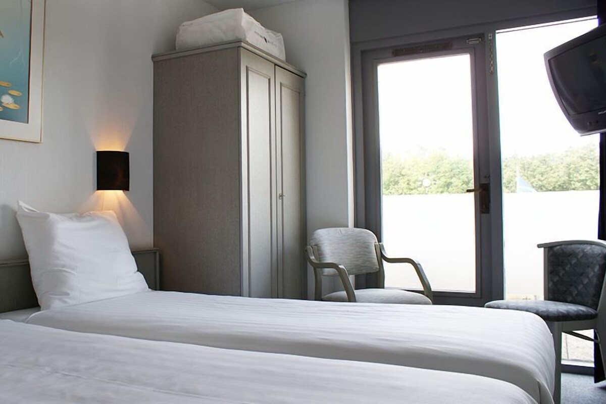 Een hotelkamer met twee bedden, een kast, een stoel en een schilderij aan de muur.