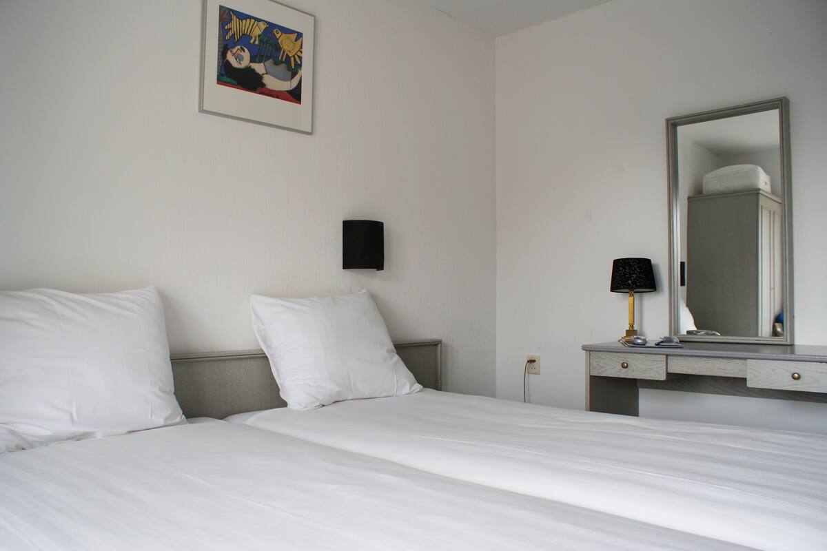 Une chambre d’hôtel avec un lit, une table de chevet, un miroir et un tableau accroché au mur.