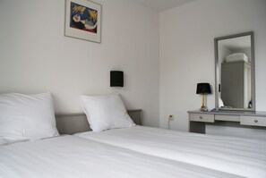 Ein Hotelzimmer mit Bett, Nachttisch, Lampe, Spiegel und einem gerahmten Bild an der Wand.