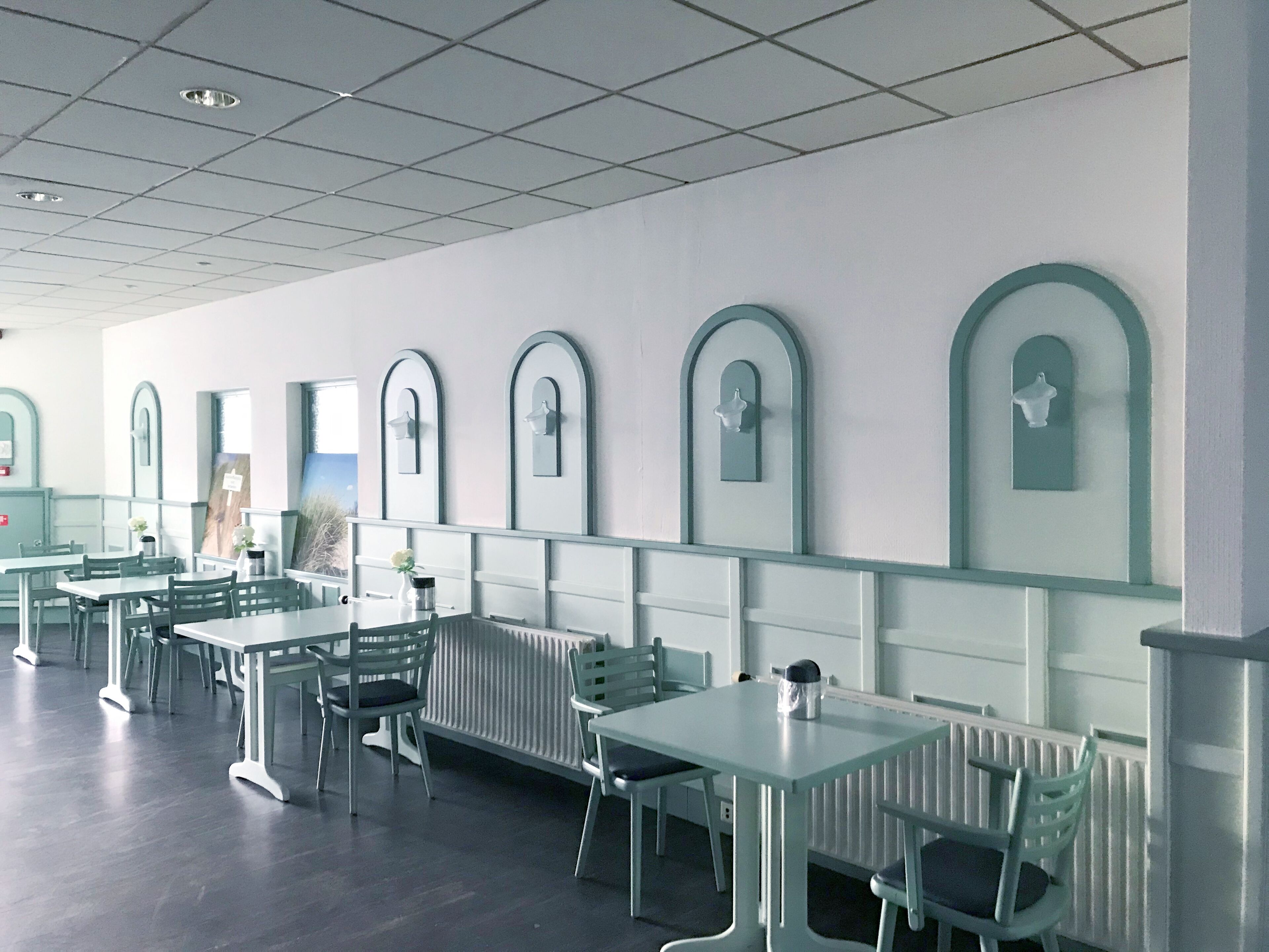 A modern dining area with white tables and chairs, a tiled ceiling, and decorative wall mirrors.