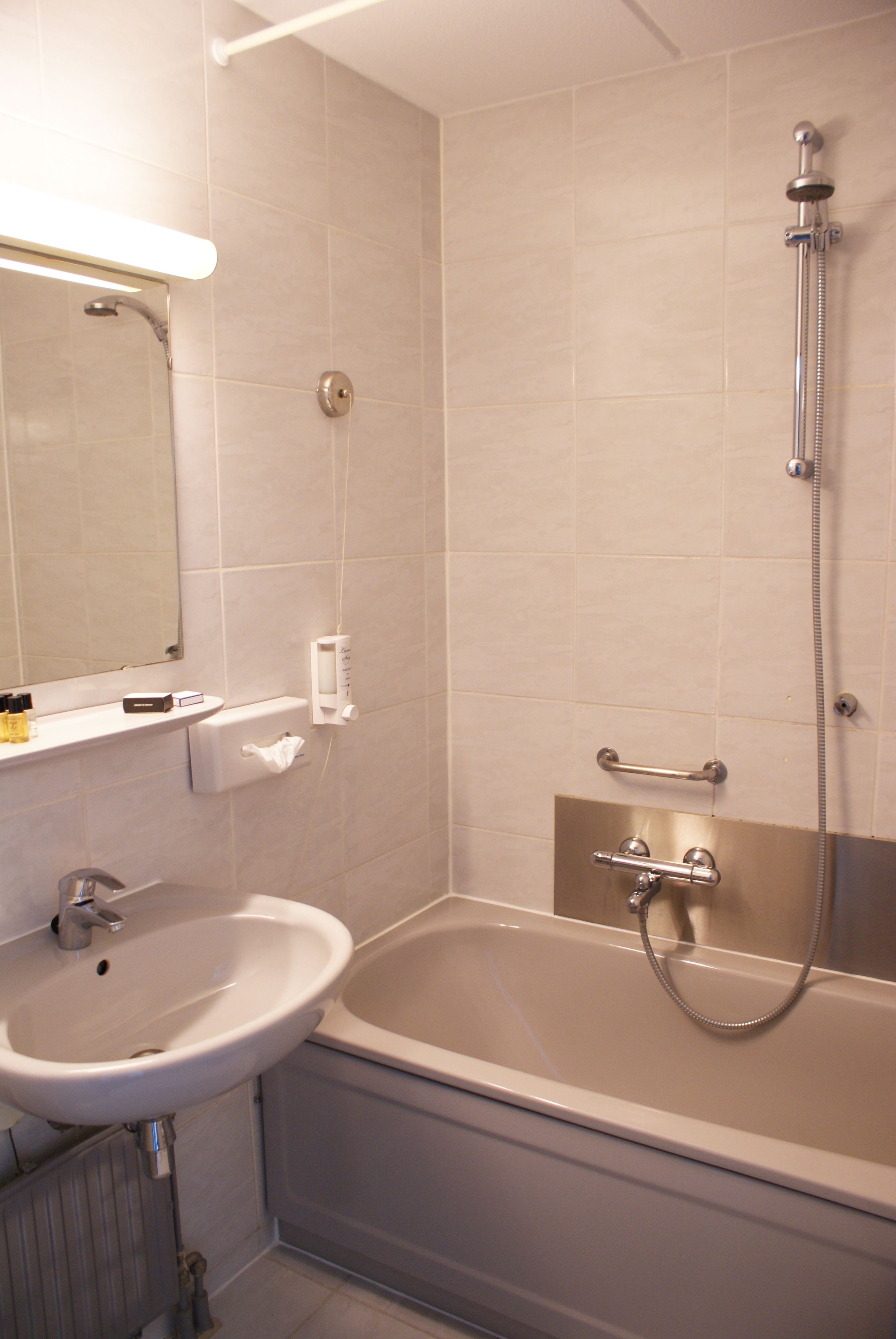 Een badkamer met een wastafel, spiegel en bad met douchekop.