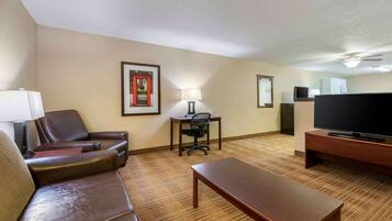 Habitación de hotel con sofá de cuero, mesa de centro de madera, escritorio y silla, televisor y lámpara.