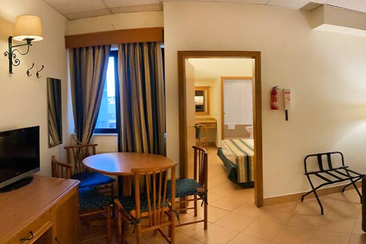 A hotel room with a dining table, chairs, a sofa, a TV, and a bed.
