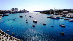 A marina with various boats docked, a clear blue sky, and buildings in the background. - Hotel Kennedy Nova (Gzira)