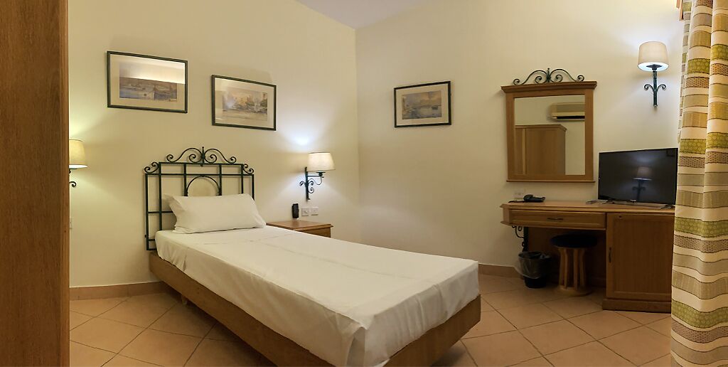 A bedroom with a bed, bedside lamps, a desk with a computer, and a mirror.