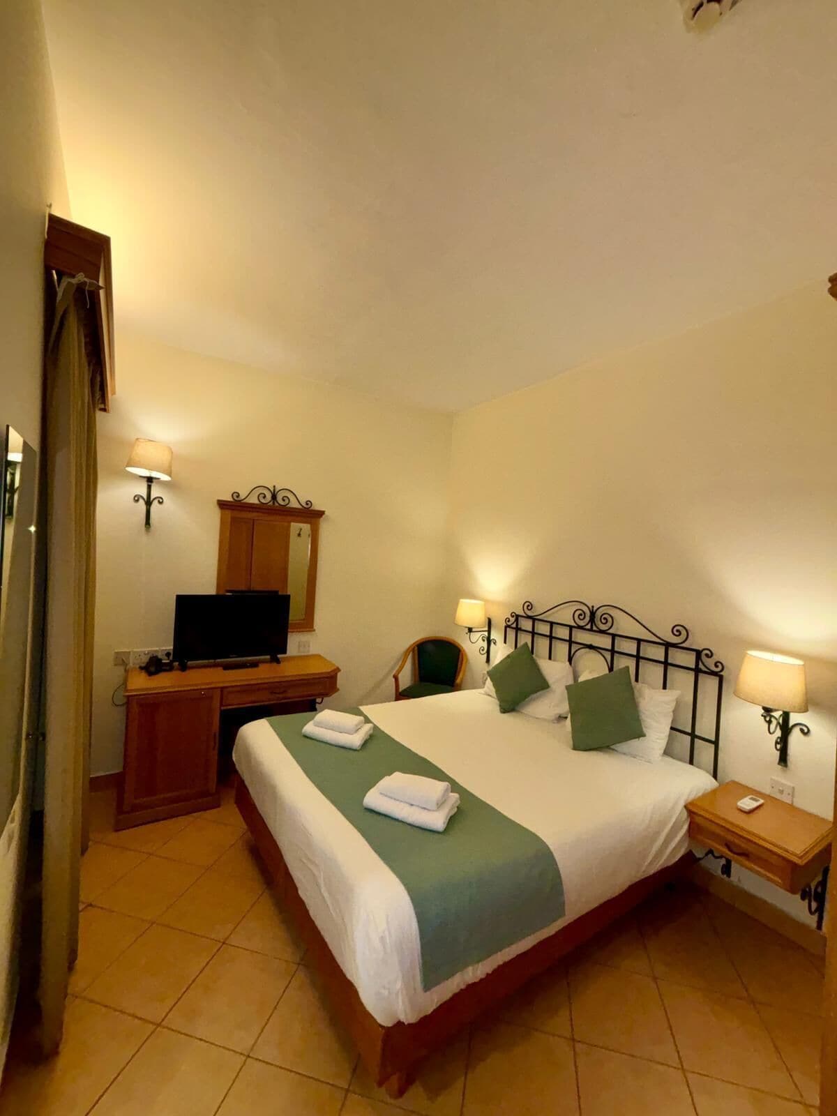 Habitación de hotel con una cama grande, un escritorio con televisor, dos lámparas de noche y un espejo en la pared.