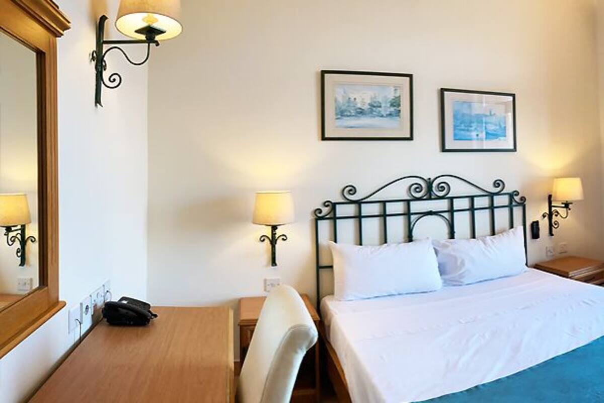 A hotel room with a bed, bedside tables, a desk, and a balcony with a view.