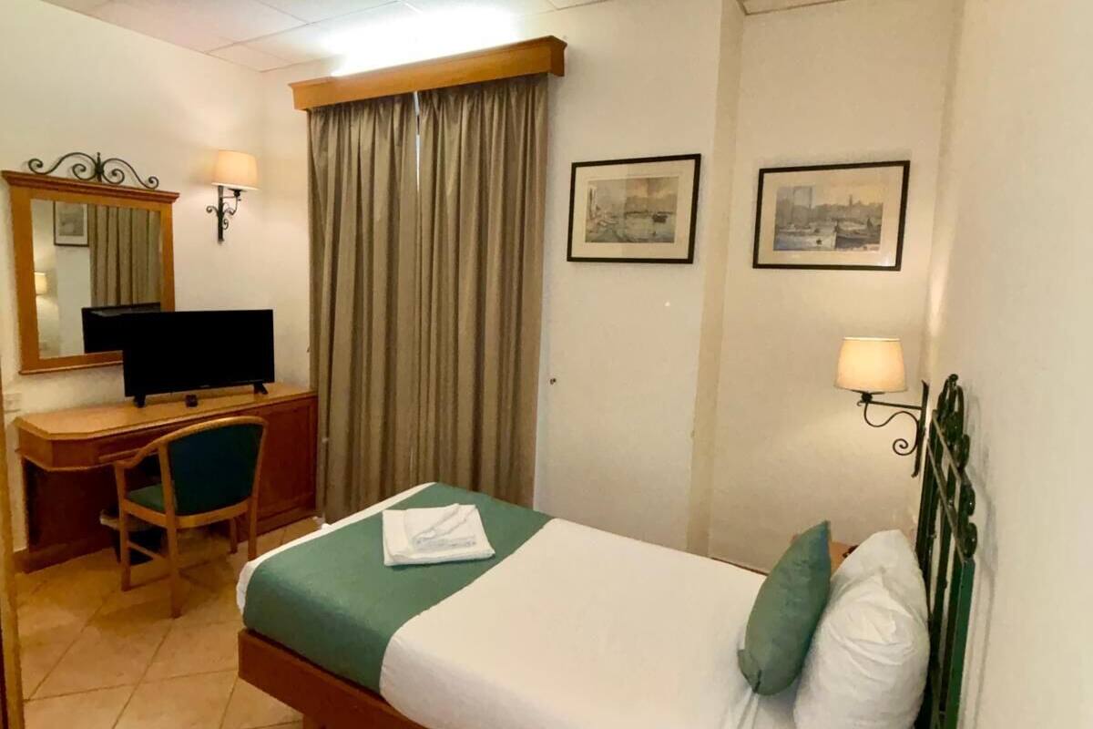 A hotel room with a bed, a desk, a chair, a television, and two framed pictures on the wall.
