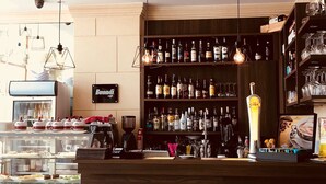A bar area with a wooden counter, shelves of liquor bottles, and a display of glasses. - Hotel Kennedy Nova (Gzira)