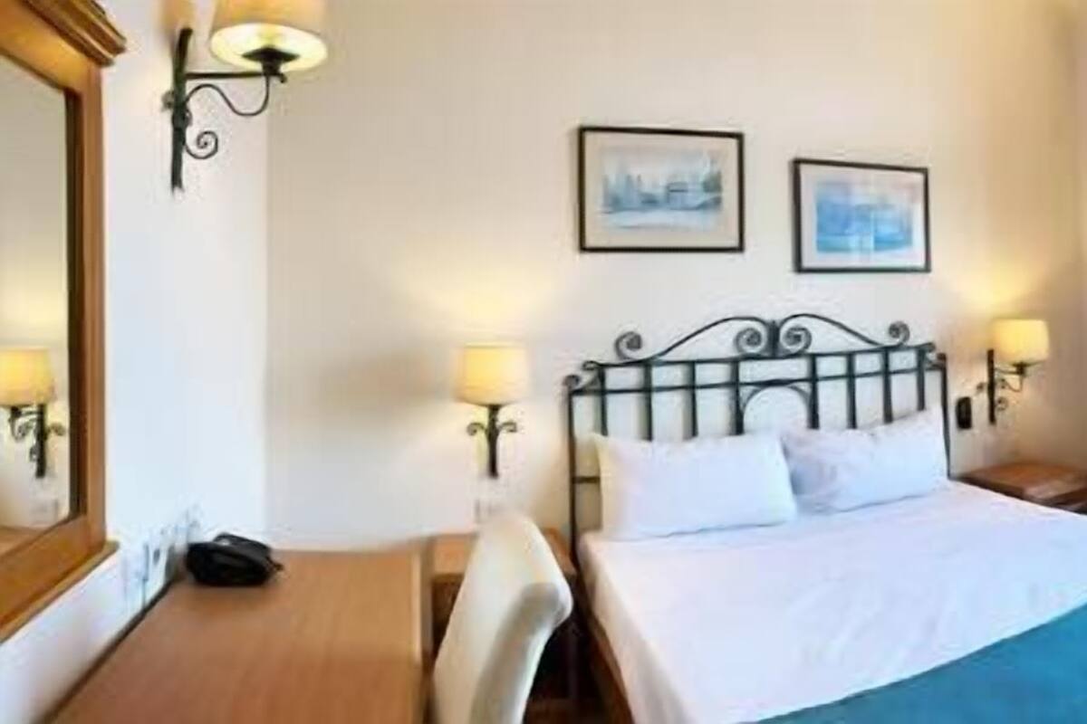 A hotel room with a bed, two wall-mounted lamps, a nightstand, a chair, and a large window with a view.