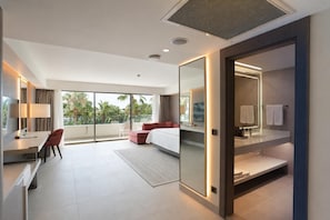 A modern hotel room with a bed, a desk, a chair, a large window with a view, and a bathroom with a mirror and towel rack. -  Mirage Park Resort - Premium All Inclusive (Kemer)