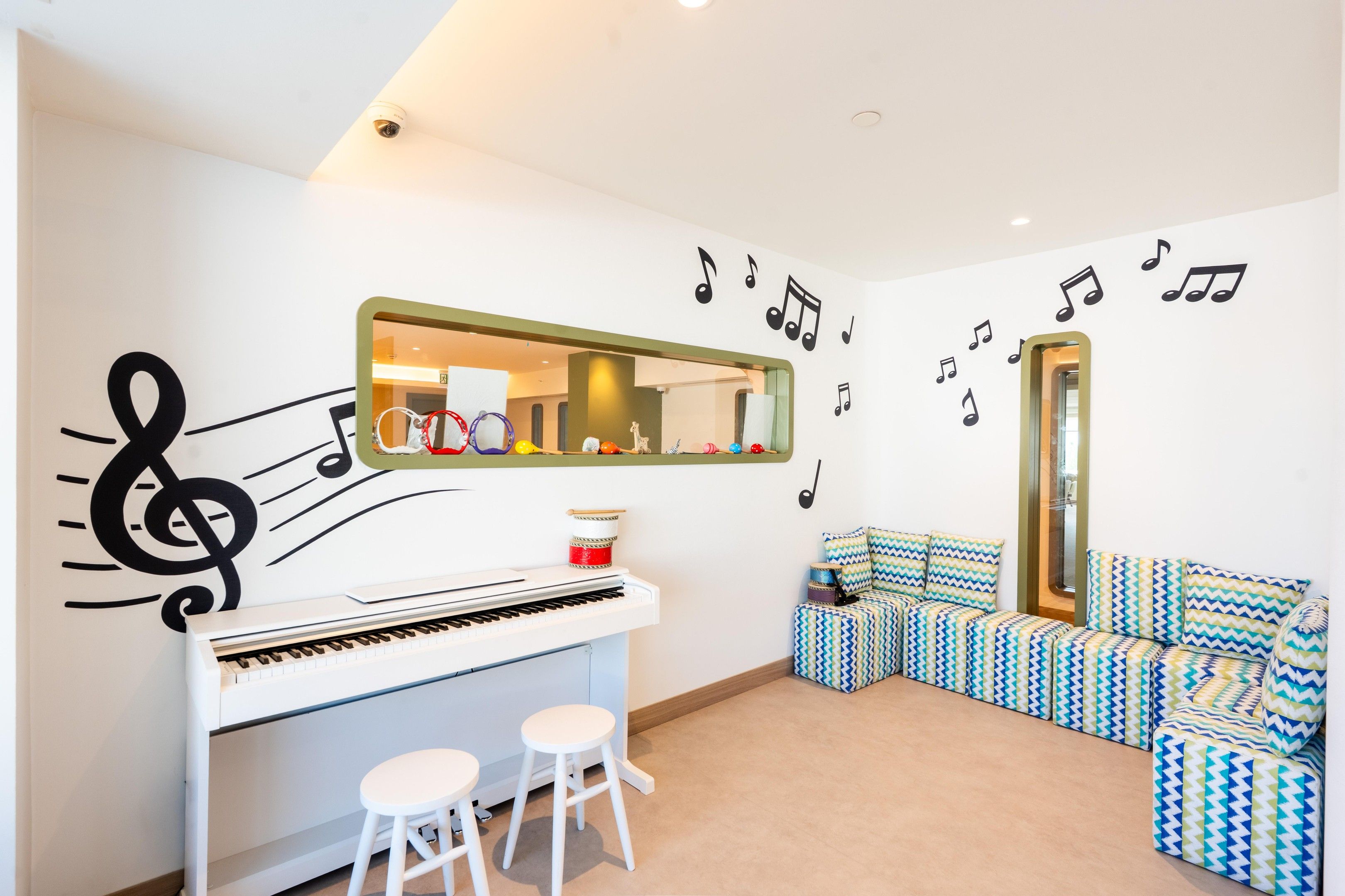 A room with a piano, stools, a mirror, a sofa, and wall decorations including musical notes and a treble clef.