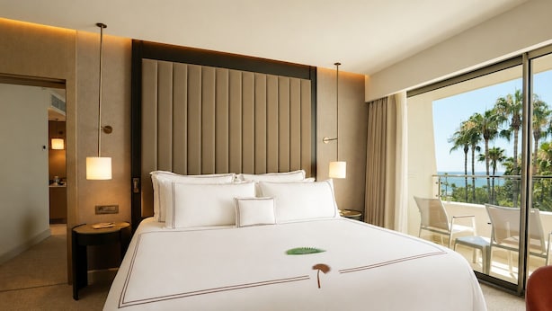 A hotel room with a large bed, a view of palm trees, and a balcony with chairs. -  Mirage Park Resort - Premium All Inclusive (Kemer)