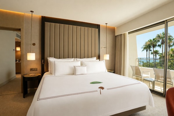 A hotel room with a large bed, a view of palm trees, and a balcony with chairs.